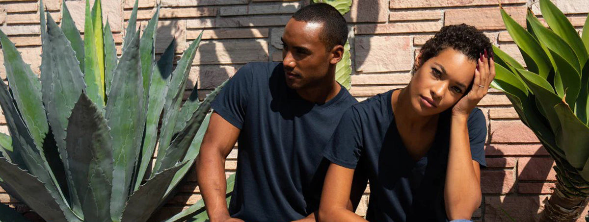 A man and woman wearing navy blue luxury organic cotton t-shirts posing by desert plants.