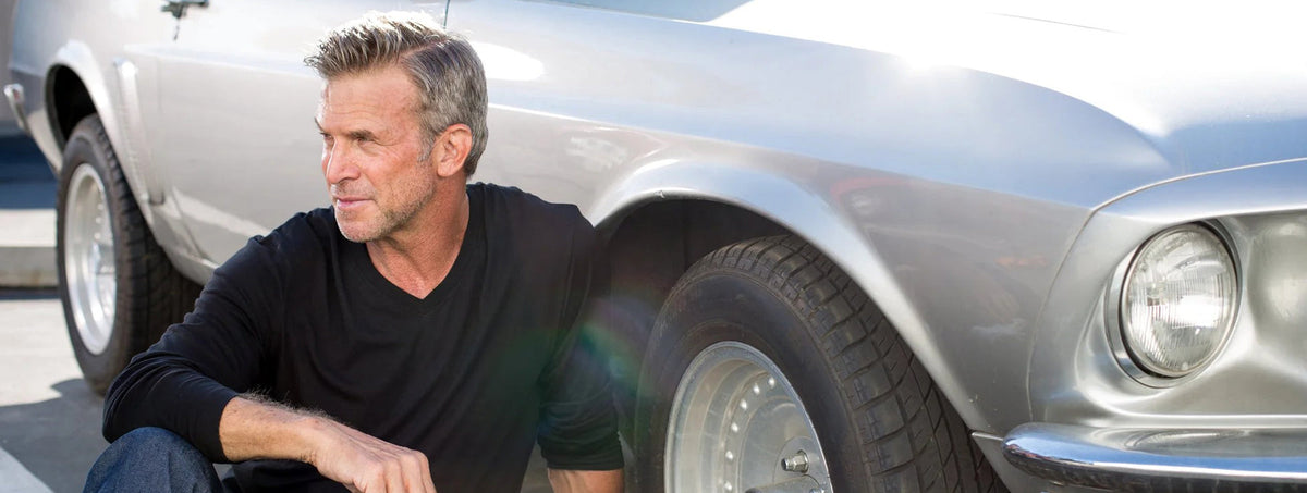Man in a black luxury V-neck long sleeve t-shirt leaning against a classic silver car.