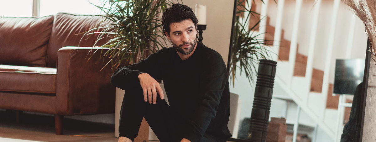 Man wearing a black long-sleeve French terry sweatshirt sitting in a living room.