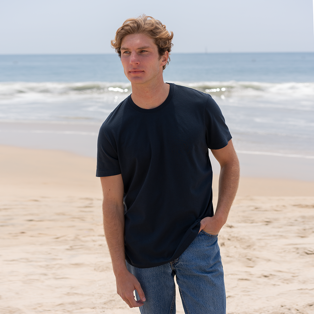 Man wearing a navy blue short sleeve organic cotton crew neck t-shirt on a sandy beach.